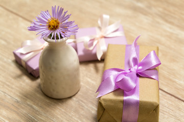 Obraz na płótnie Canvas Purple spring flowers in a white vase on a wooden table. Gift box wrapped in craft paper with ribbon