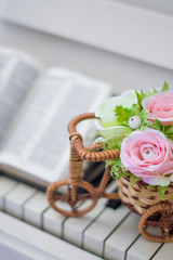 Fototapeta na wymiar Decorative flowers (roses) in a wicker bicycle on the piano and the Bible. Topiary. Wedding decor, decoration. Close-up.