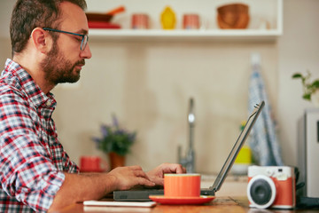 Modern bearded man using cellphone and drinking coffee with laptop.