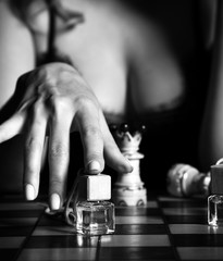 Black and white. Sexy woman in lace nightdress with deep neckline playing chess with perfume...