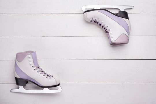 Close-up photo of professional ice skates lying on a white wooden background.