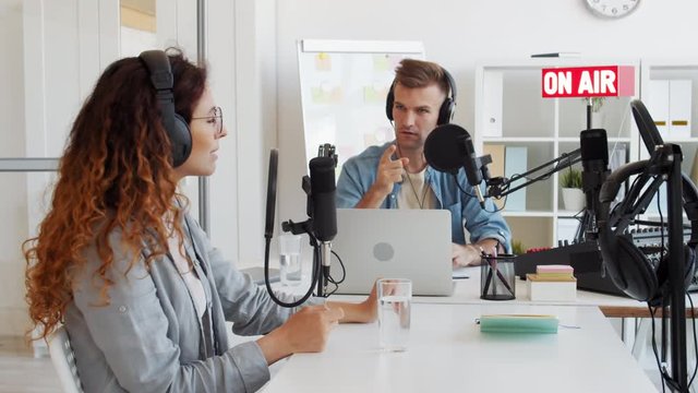 Lockdown of male Caucasian radio host having discussion on air with female redheaded interlocutor sitting nearby in studio