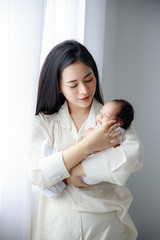 Asian young mother is carrying a newborn lovely baby in white bed room. Duty of the wife to raise children. Mother and child concept.
