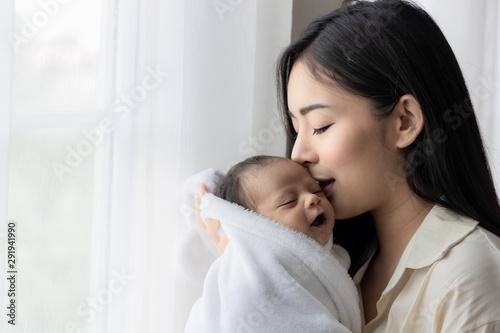 Portrait of asian young mother kissing her cute newborn baby in white bed room. Wife and mother's day concept.