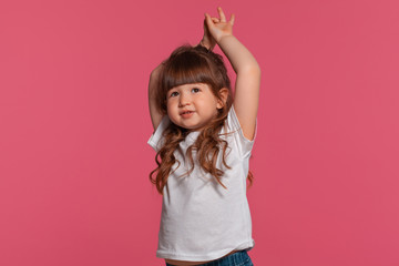 Close-up portrait of a little brunette girl dressed in a white t-shirt posing against a pink studio background. Sincere emotions concept.