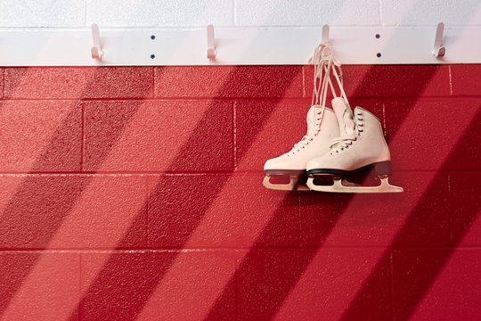 Figure skates hanging over gradient red wall in locker room with copy space