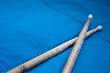 Close up crossed worn out wooden drumsticks over blue bedspread. Ideal for drummers practicing in...