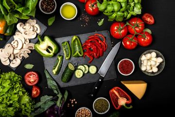 Raw ingredients for cooking vegetarian healthy food. Flat lay of vegetables and cheese on a black background.