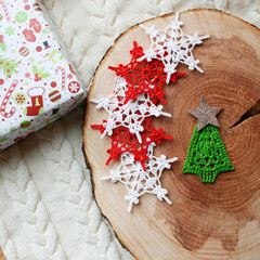 Snowflakes crocheted in different colors on a wooden log on a white knitted background. Top view. The concept of winter holidays, Christmas, New year.