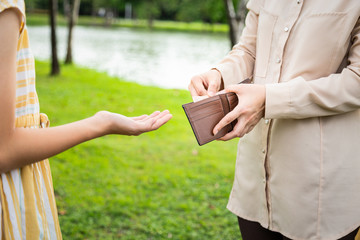 Closeup hands of asian woman hands open wallet,mother or guardian giving pocket money to daughter ,child girl demanding money,allowance,parent pulls out money from wallet to give her in outdoor park