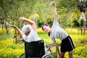 Asian senior grandmother sit relax,exercise in wheelchair with beautiful child girl granddaughter having fun enjoy together in outdoor flower garden for some fresh air,health care,family relationships