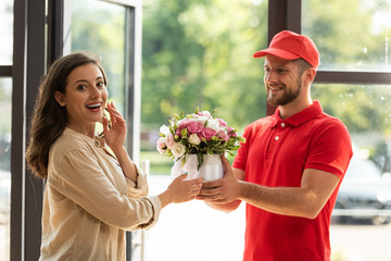 bearded and happy delivery man giving flowers to beautiful woman