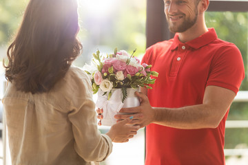 cropped view of happy delivery man giving flowers to woman