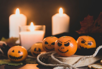 Happy Halloween citrus, tangerines painted with scary, funny faces. Dark photo with candles. Alternatives to traditional Halloween pumpkins.