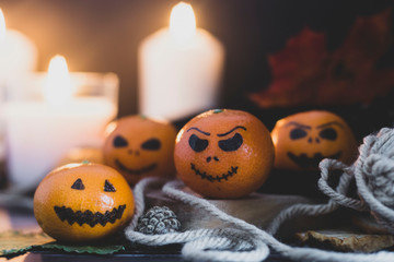 Happy Halloween citrus, tangerines painted with scary, funny faces. Dark photo with candles. Alternatives to traditional Halloween pumpkins.