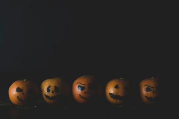 Happy Halloween citrus, tangerines painted with scary, funny faces. Dark photo with copy space.