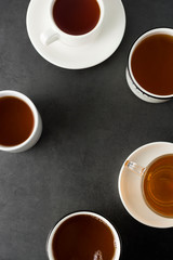 Top view of many cups, mugs with hot tea drink on dark background, copy space. Tea time or tea brake. Autumn beverage. Toned image with tea cups.