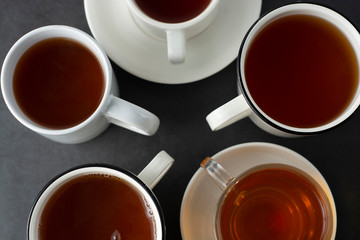 Top view of many cups, mugs with hot tea drink on dark background, copy space. Tea time or tea brake. Autumn beverage. Toned image with tea cups.