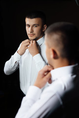The groom is dressed at home in a suit. Portrait handsome groom in suit near mirror. Fashion groom. Handsome groom on his wedding day.