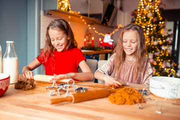 Little girls making Christmas gingerbread house at fireplace in decorated living room.