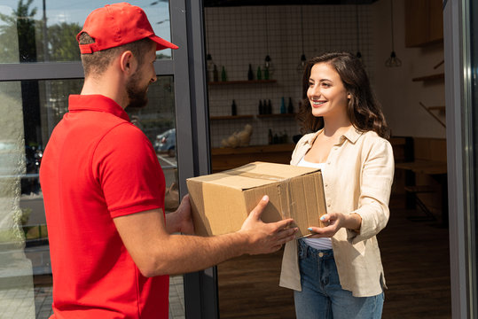 Bearded Delivery Man Giving Cardboard Box To Cheerful Woman