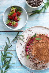 A whole delicious chocolate cake with chocolate chips and strawberries in a composition with willow twigs. View from above.