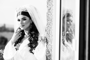Reflection in the window. Portrait of an incredibly beautiful girl in robe and wedding make-up, beautiful eyes, painted lips and a sincere smile and waiting for the wedding. Black and white