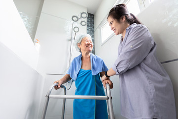 Asian daughter or female care assistant service, help,support senior woman taking a shower in bathroom,care closely,happy mother walking with walker in bathroom at home,safety of elderly people 