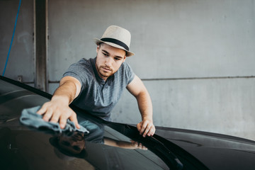 Young handsome man with hat cleaning car with rag, car detailing (or valeting) concept.