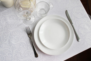 dining table with a white tablecloth and a white plate. photo of a table with utensils top view.