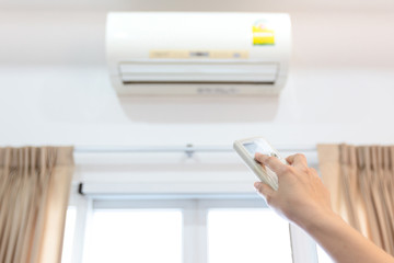 Woman holding a remote control with air conditioner on a white wall background,hand turn off the air conditioner with remote control after use to energy saving,save electricity bill and global warming