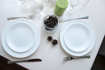 table setting for two persons with cutlery, white plates on a light tablecloth, view from the top.