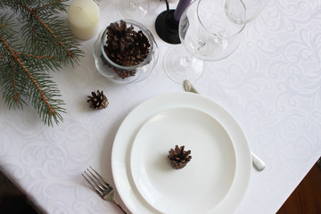 Festive table setting among winter decorations and white candles. Top view, flat lay, concept of christmas or thanksgiving family dinner.