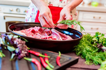 Cook adds rosemary to raw lamb ribs on frying pan close up