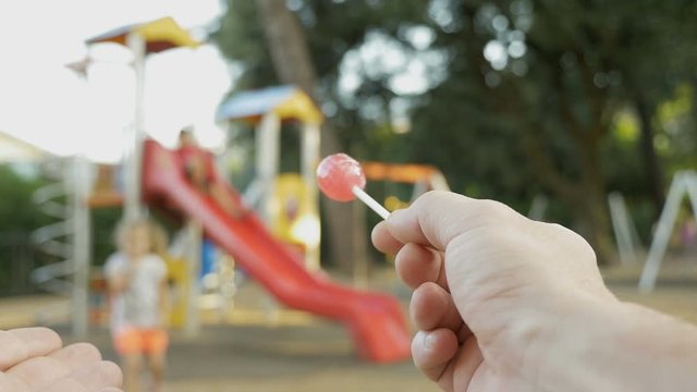 Attempt of child abduction. Stranger with candy in hand tries to theft a child. Person spying on kids on the playground and calls a child to himself. Child abduction, human kidnapping concept.
