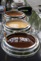 Dark, white and brown liquid chocolate in metal containers. Street point of sale..