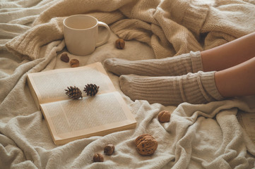 Cozy Autumn winter evening , warm woolen socks. Woman is lying feet up on white shaggy blanket and reading book