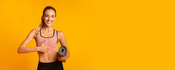 Girl Holding Rolling Mat Gesturing Thumbs-Up On Yellow Background, Panorama