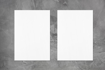 Two empty white vertical rectangle poster mockups with soft shadows on dark grey concrete background. Flat lay, top view