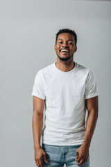 African American man in white T-short laughing and looking at camera isolated on grey