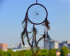 A Dreamcatcher suspended from a window.Outside, the sky is overcast and the city is blurred.