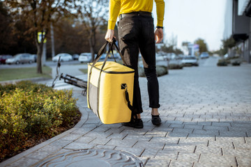 Courier carrying yellow thermal bag, delivering food in the city, close-up view with copy space. Delivery service concept