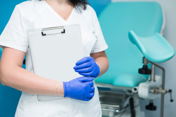 Caucasian female gynecologist in white coat and blue sterile gloves holding a paper tablet