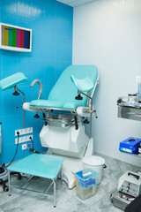 a blue gynecological chair in the gynecologist’s office stands next to a table on which sterile medical instruments are placed