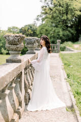 Amazing brunette Chinese Asian bride in luxury wedding dress, posing at old castle background, standing near the stone railings, wedding photo, European city, wedding day, portrait