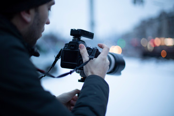 photo of a man from behind with a camera in his hands photographing winter city streets, a photographer against the background of an evening city. selective focus, noise effect