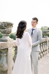 wedding beautiful Chinese couple in the sunny day in ancient castle, posing and holding hands near the old railings