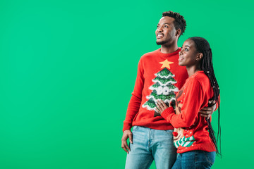 African American man hugging woman in red Christmas sweater and looking away isolated on green