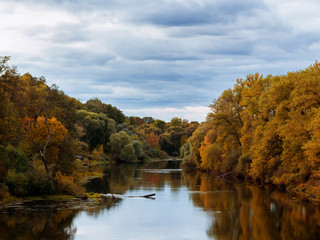 Autumn landscape in cloudy weather. Colorful forest by the river