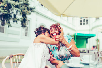 Senior woman whispering something to her friends ear in a cafe